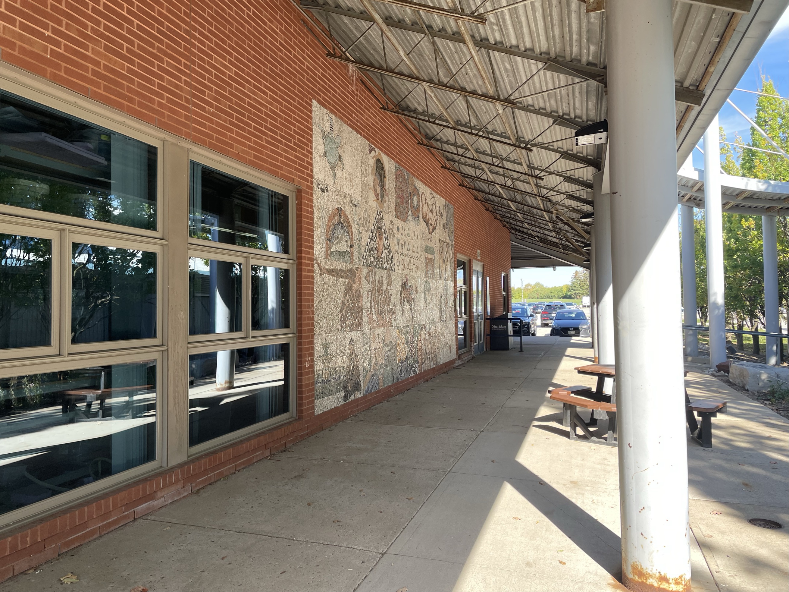 This is a mosiac placed outside the AS building. It's used as decoration and an area for students to sit in. It appears materials such as stone, metal, glass, and wood are used to construct the area.